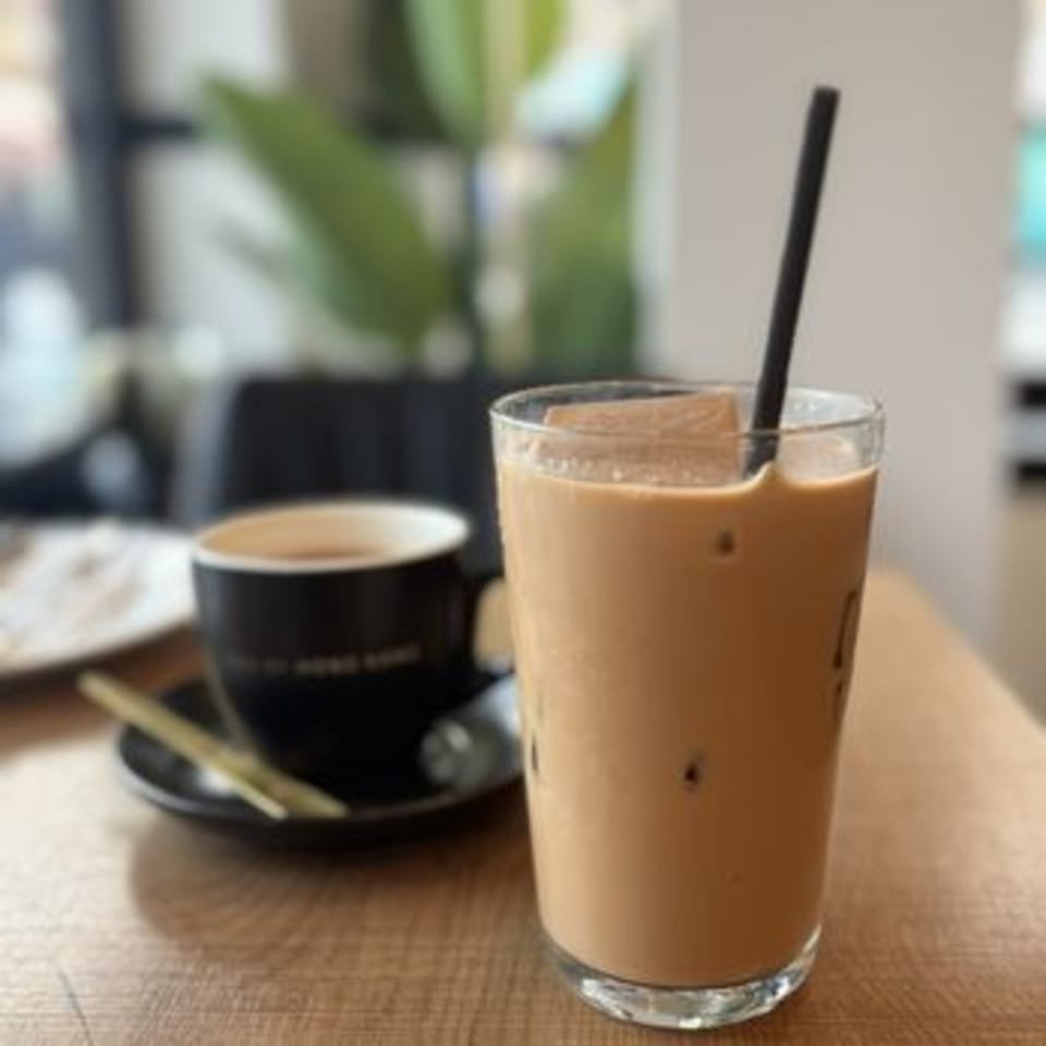 Iced milk tea with a straw and a hot coffee cup on a wooden table at 606.