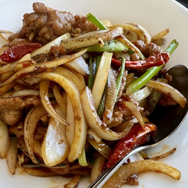Close-up of Chinese stir-fried beef with onions, green onions, and red chili peppers.