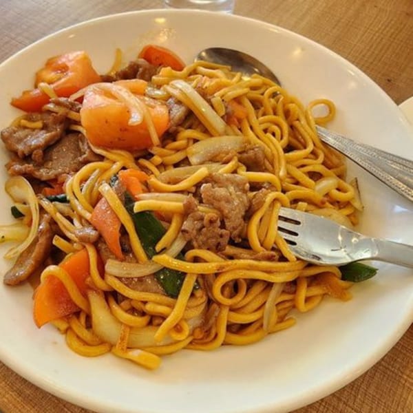 A plate of Chinese chow mein with beef, tomatoes, onions, and green vegetables.