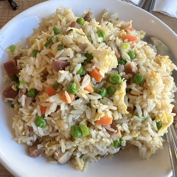 A white bowl filled with Chinese fried rice, featuring peas, carrots, egg, and meat.