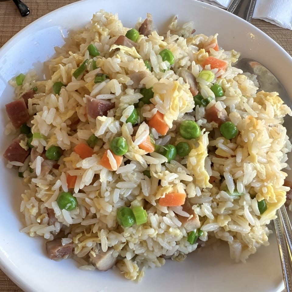 A white bowl filled with Chinese fried rice, featuring peas, carrots, egg, and meat.
