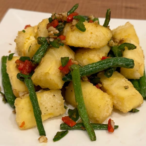 Crispy fried tofu cubes with green beans, red peppers, and garlic on a white plate.