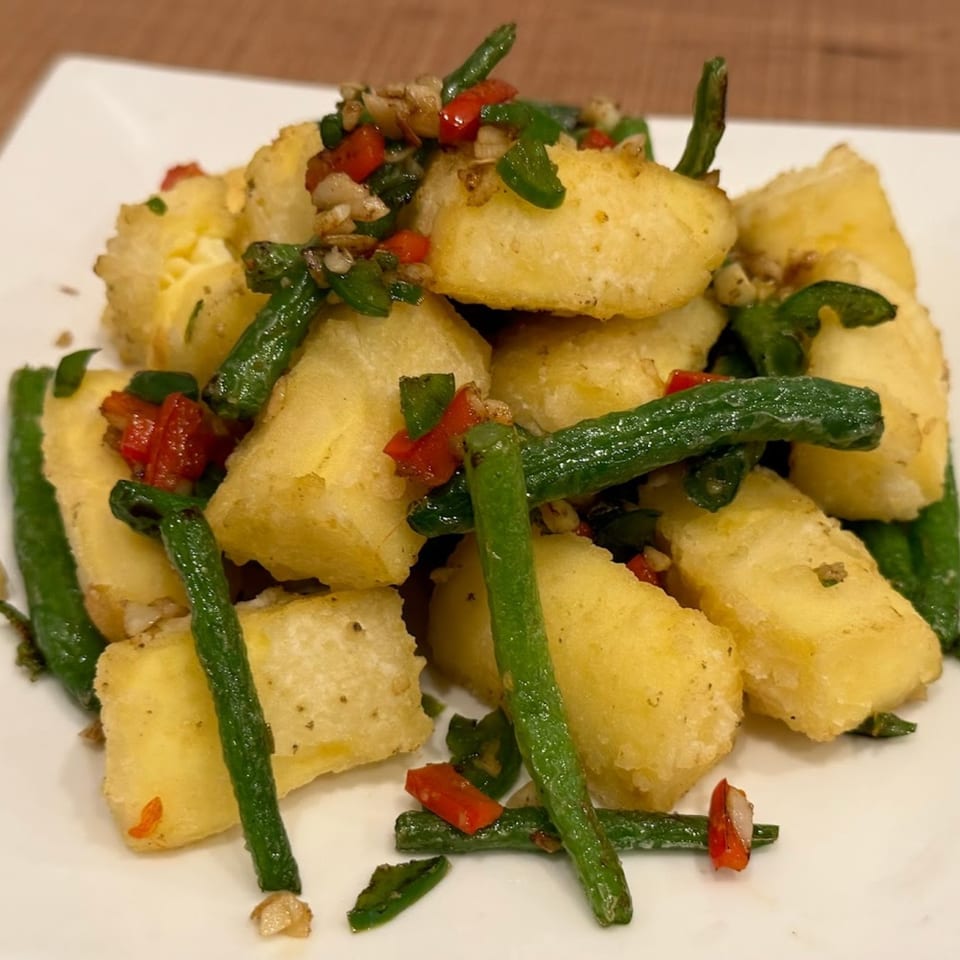Crispy fried tofu cubes with green beans, red peppers, and garlic on a white plate.