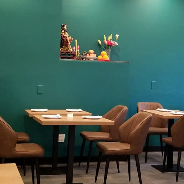 Interior of 606 Chinese restaurant with teal walls, wooden tables, brown chairs, and a small shrine.