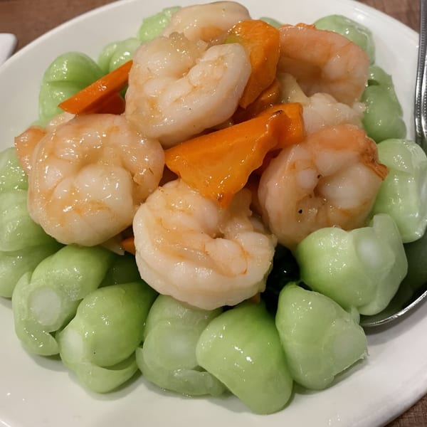 Shrimp and bright green vegetables with orange carrot slices in a white bowl.