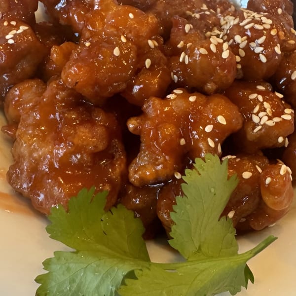 Close-up of 606's Chinese orange chicken, glistening with sauce, topped with sesame seeds and cilantro.
