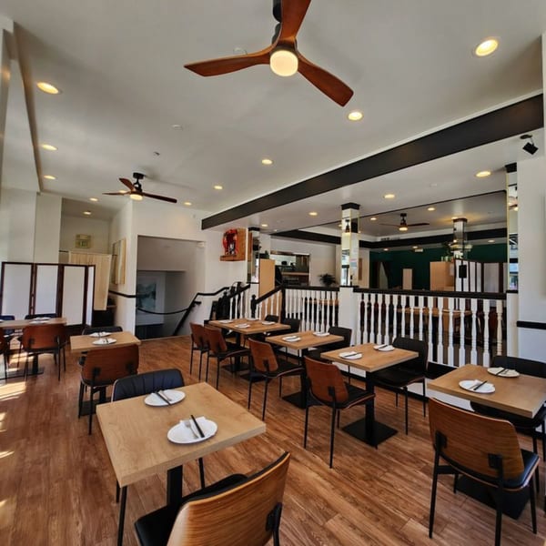 The 606 restaurant interior features wooden tables, modern chairs, and ceiling fans in a brightly lit dining area.