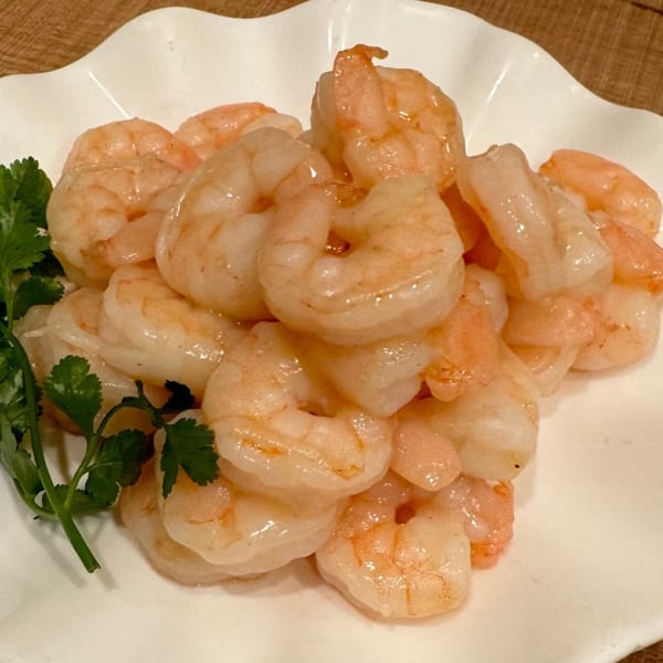 A white plate piled high with cooked shrimp, garnished with fresh green cilantro.