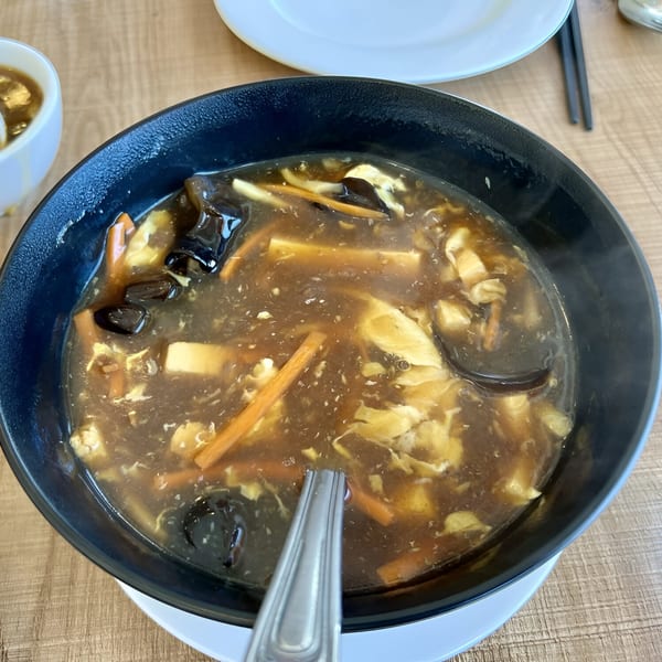 A steaming bowl of 606 Chinese hot and sour soup with tofu, mushrooms, and carrots.