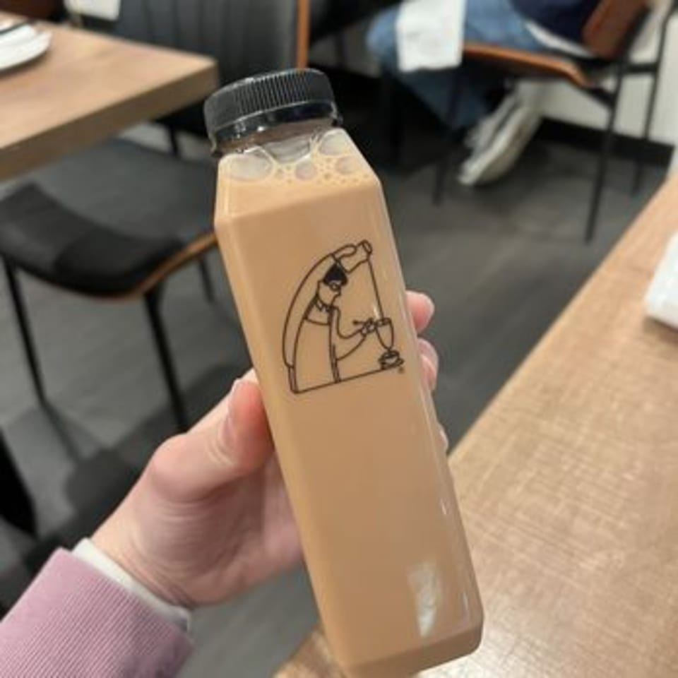 Hand holding a bottled milk tea with a black cap and a cartoon chef logo.