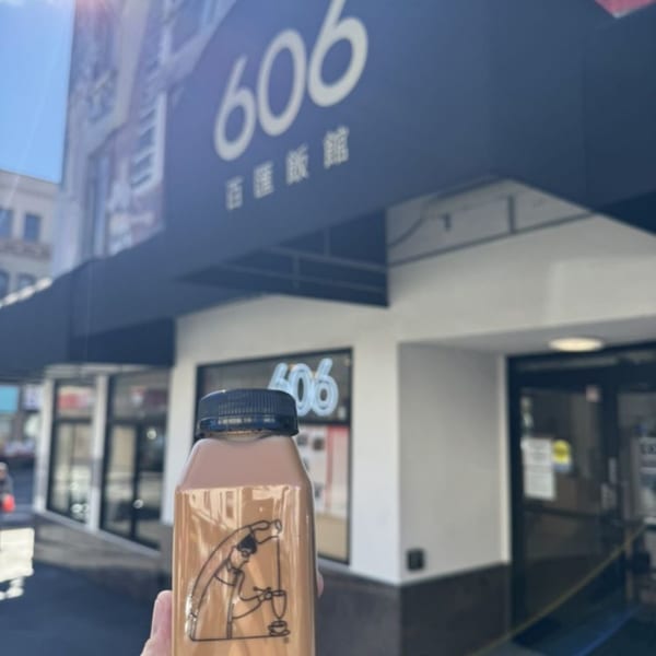 Hand holding a bottled drink with a cartoon design in front of the 606 restaurant entrance.