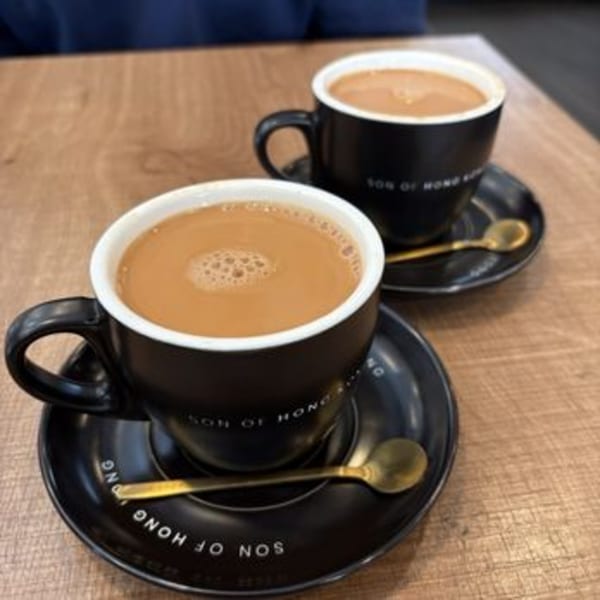 Two black mugs of Hong Kong-style milk tea with golden spoons on a wooden table.