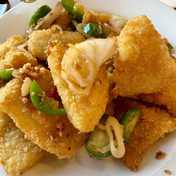 Crispy fried fish pieces with sliced green peppers and onions on a white plate.